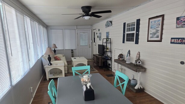 Un comedor con mesa y sillas, un ventilador de techo y un televisor al fondo.