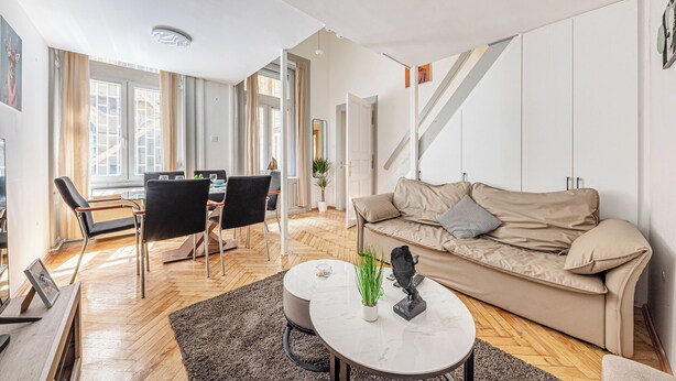 A modern living room with a sofa, coffee table, and chairs. There is a staircase and a door leading to another room.