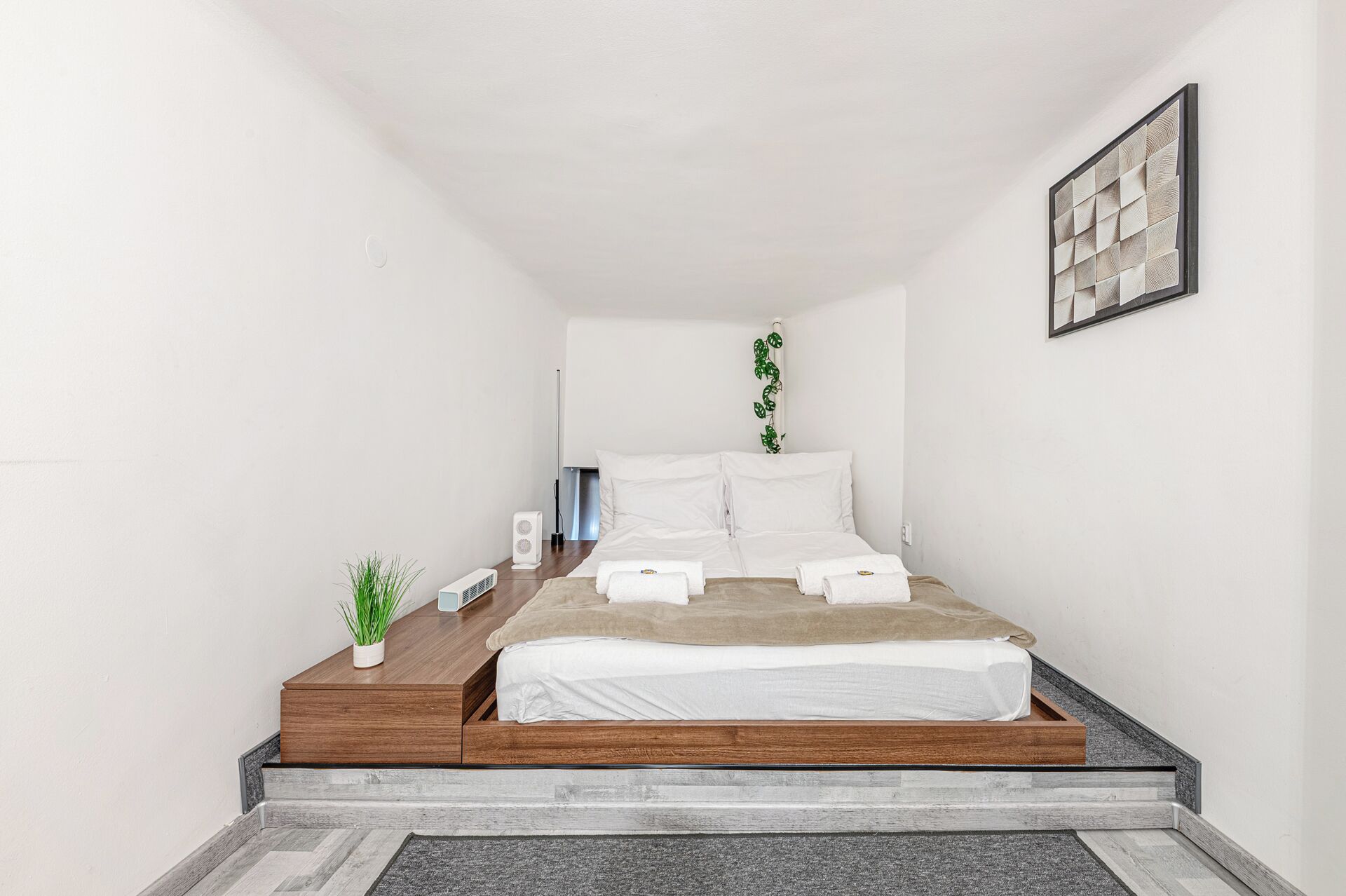 A modern bedroom with a bed, bedside tables, a small plant, and a wall-mounted artwork.