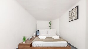 A modern bedroom with a bed, bedside tables, a small plant, and a wall-mounted artwork.