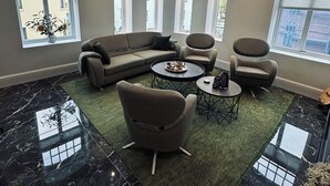 Una sala de estar moderna con un sofá modular, una mesa de centro redonda y sillones. Amplias ventanas ofrecen luz natural y vistas de la ciudad.