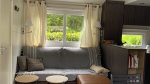 Un espacio habitable compacto con sofá, dos mesitas, una mesa de comedor y una zona de cocina con armarios y ventana.
