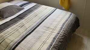 Un dormitorio con cama, una ventana con cortinas amarillas, un estante en la pared y una mesita de noche pequeña.