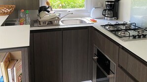 Una cocina moderna con armarios de madera oscura, estufa a gas, cafetera y ventana con vista a zonas verdes.
