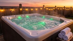 A hot tub with green lights, surrounded by a wooden fence and string lights, with towels on a stool. - Jungle themed house for groups up to 13 (Edmonton)