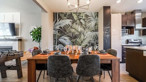 A modern dining area with a wooden table set for four, surrounded by dark chairs. A large mural of a jungle scene adorns the wall behind the table. - Jungle themed house for groups up to 13 (Edmonton)