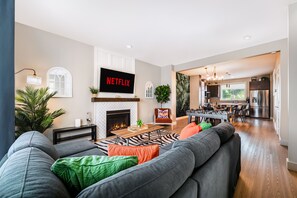 Un soggiorno moderno con camino, una TV a schermo piatto che mostra 'NETFLIX' e un'area pranzo con cucina sullo sfondo.
