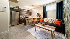 A modern kitchen with a refrigerator, microwave, and island. There is a dining area with a sofa and chairs. The room has a large window with curtains. - Jungle themed house for groups up to 13 (Edmonton)
