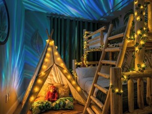 A room with a bed, a wooden ladder, a teepee with lights, and a giraffe plush toy.