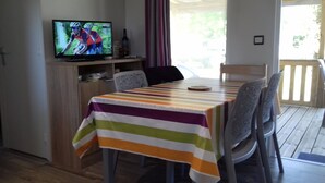 A dining area with a striped tablecloth, chairs, a television displaying a cycling event, and a bottle on the shelf.