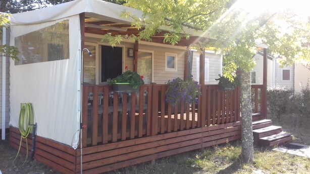 A covered outdoor area with a wooden deck, a covered seating area, and a small porch with steps leading up to it.