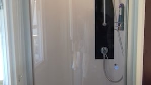A shower with a glass door, a handheld showerhead, and a wall-mounted faucet.