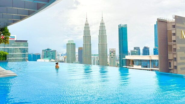 Een groot binnenzwembad met een stadsachtergrond, waaronder de Petronas Towers.