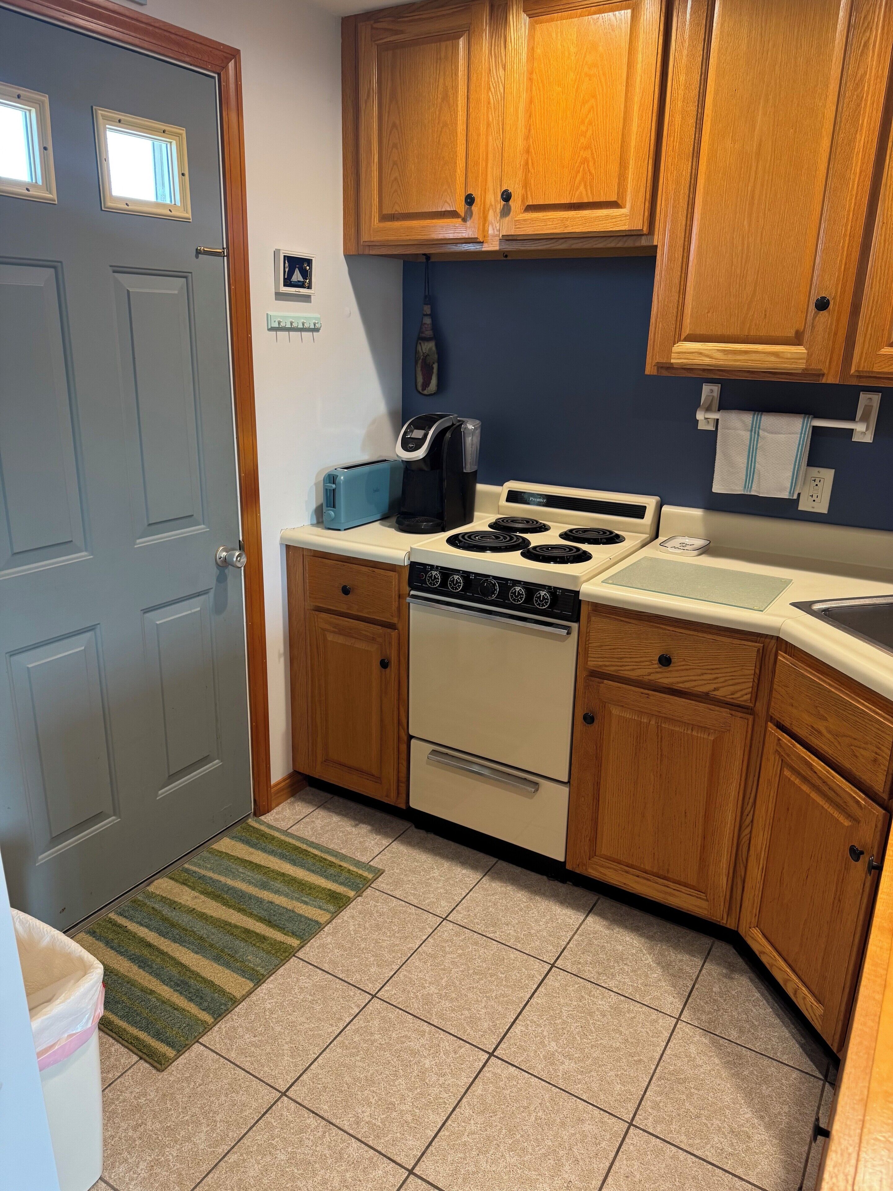 A compact kitchen with wooden cabinets, a stove, a toaster, and a coffee maker.