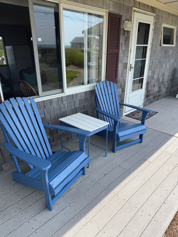 A covered porch with two blue Adirondack chairs and a small table.