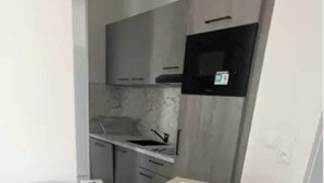 Une cuisine avec des meubles gris, un micro-ondes noir et un plan de travail blanc.