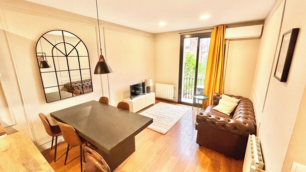 A modern living room with a dining area, a sofa, a TV, and a large window with curtains. - Nice apartment in Gracia neighborhood (Barcelona)