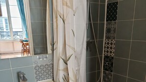 A bathroom with a white sink, wooden vanity, and a shower with patterned tiles. - Cosy studio in the heart of Paris (Paris)
