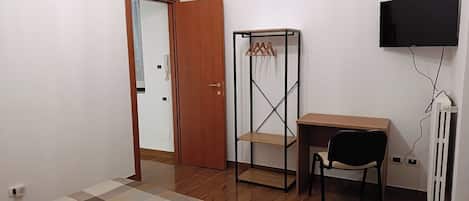 A bedroom with a bed, a desk, a chair, a wardrobe, a TV, and a radiator.