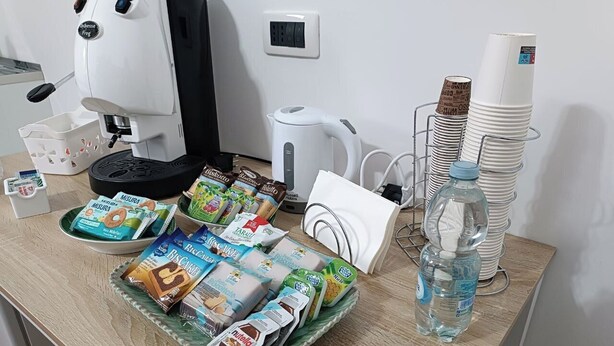 A breakfast setup with a coffee machine, tea kettle, stacked paper cups, and various packaged food items on a wooden table.
