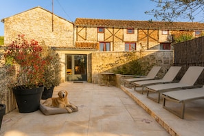 A stone building with a tiled roof, a dog lying on a mat, and outdoor seating.
