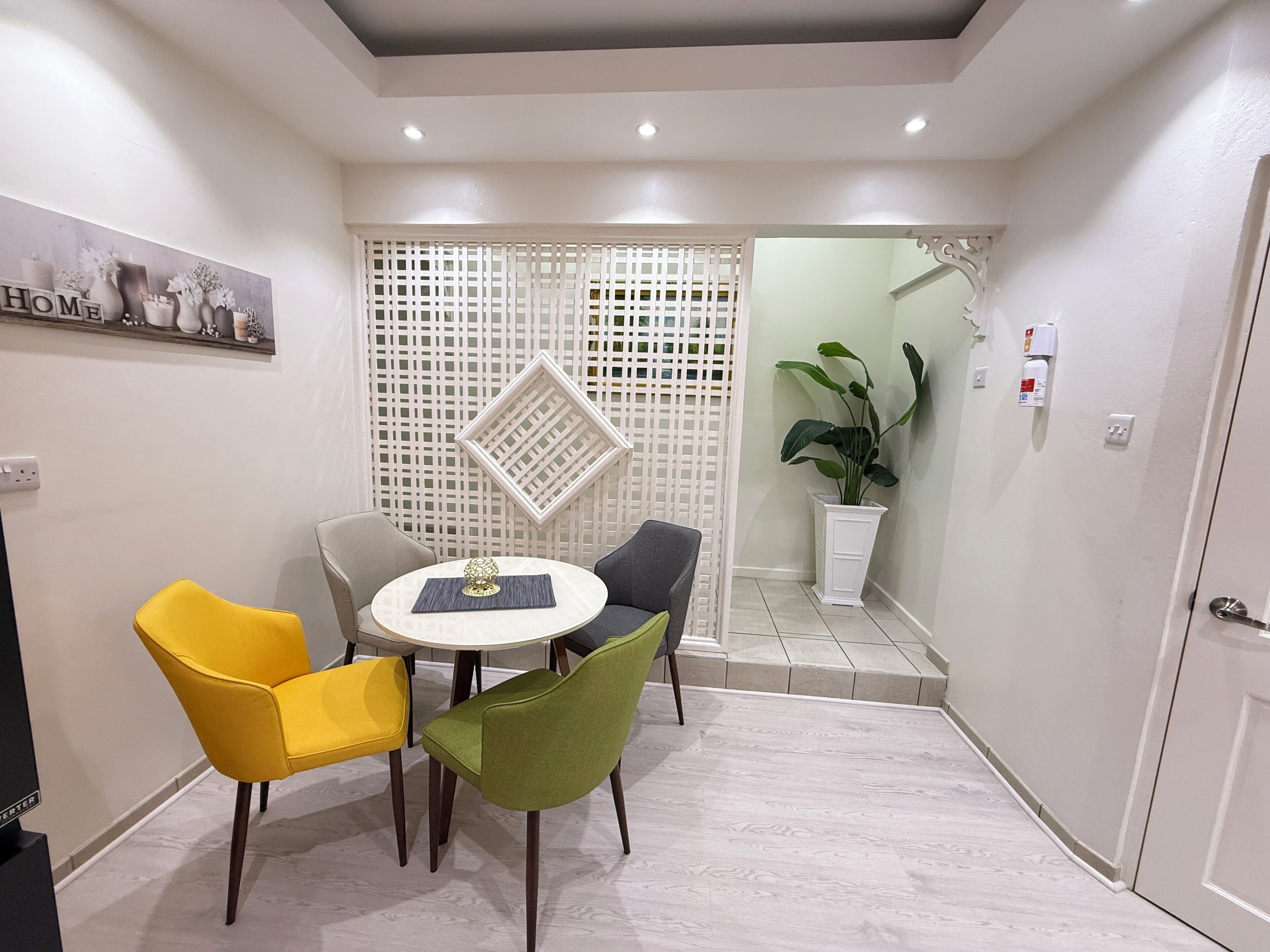 Un petit coin repas avec une table ronde, quatre chaises, un mur décoratif et une plante en pot.
