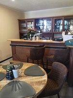 Una zona de bar con mostrador de madera, taburetes y un espacio de estar con una mesa redonda y sillas acolchadas.