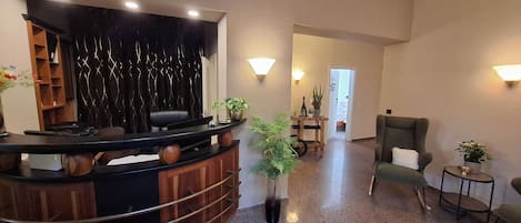 Un área de recepción con un mostrador curvo de madera, un telón negro de fondo y tres cuadros en la pared.