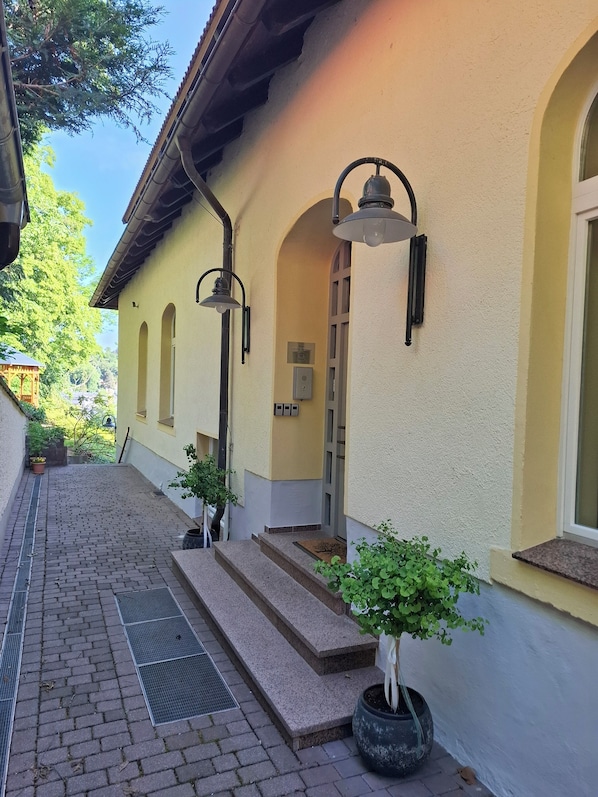 A building with a yellow facade, a covered entrance, and a small garden area with potted plants. - Hotel Burgblick Meissen (Meißen)
