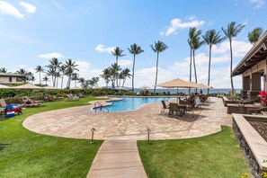 Un área de piscina con sillones de descanso, una piscina pequeña y palmeras.