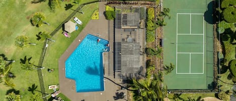An aerial view of a property with a swimming pool, tennis court, and surrounding greenery.