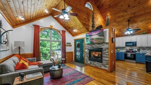 Ein geräumiges Wohnzimmer mit Kamin, Holzboden und einem großen Fenster mit Blick auf Grünflächen.