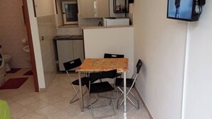 A compact living space with a kitchenette, a dining area with a table and chairs, and a television mounted on the wall.