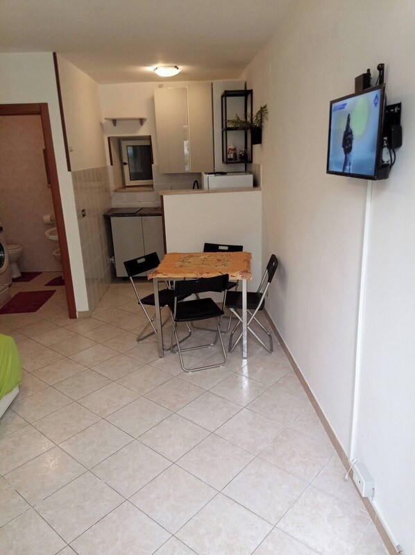Un espacio habitable compacto con kitchenette, una zona de comedor con mesa y sillas, y un televisor montado en la pared.
