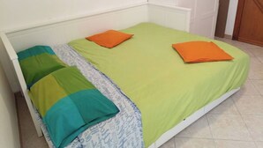 A single bed with a green bedspread and two orange pillows.