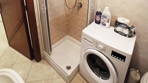 A shower with a glass door, a washing machine, and toiletries on a counter.