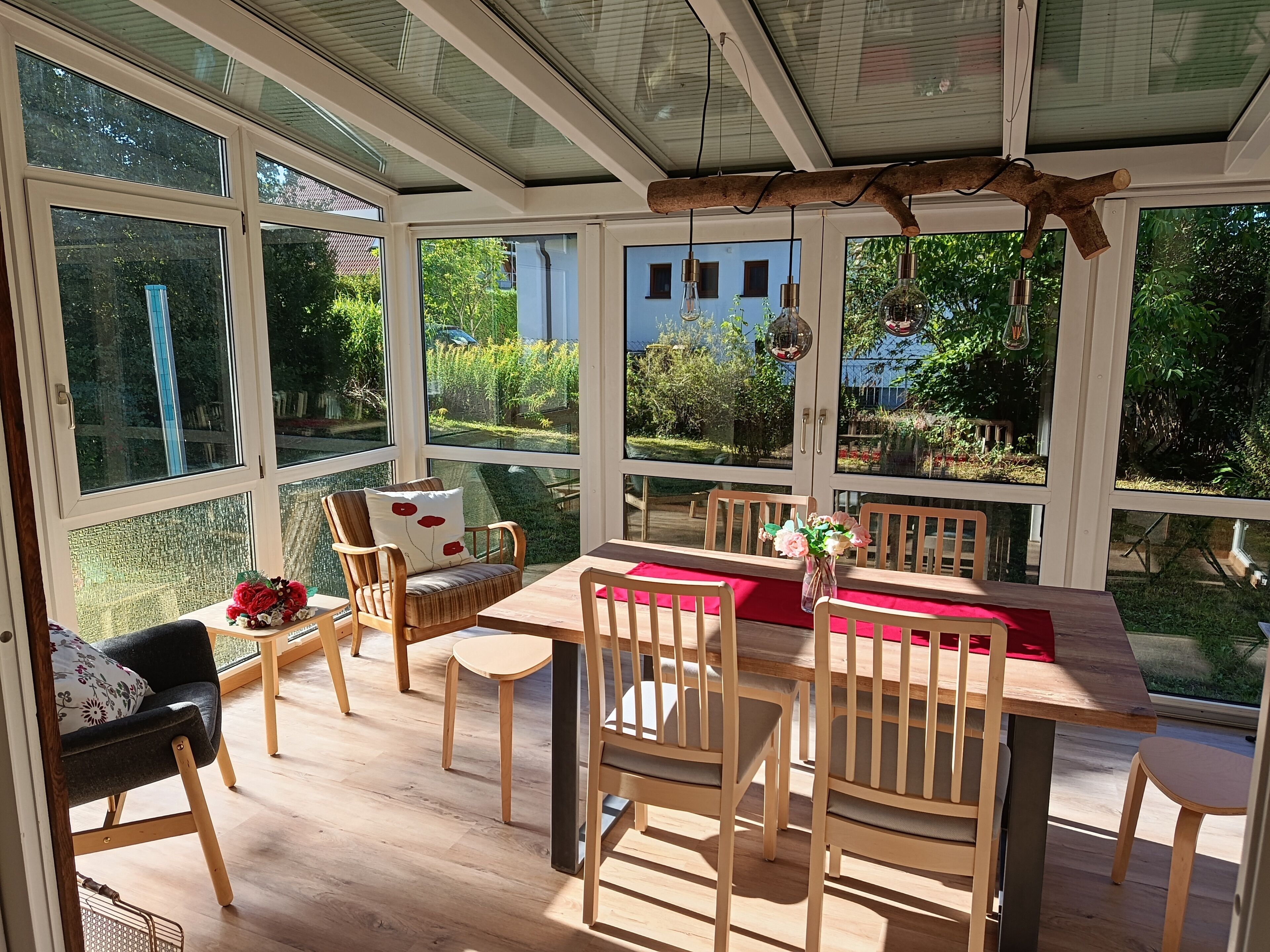 A sunroom with a wooden table and chairs, large windows, and a view of the garden.