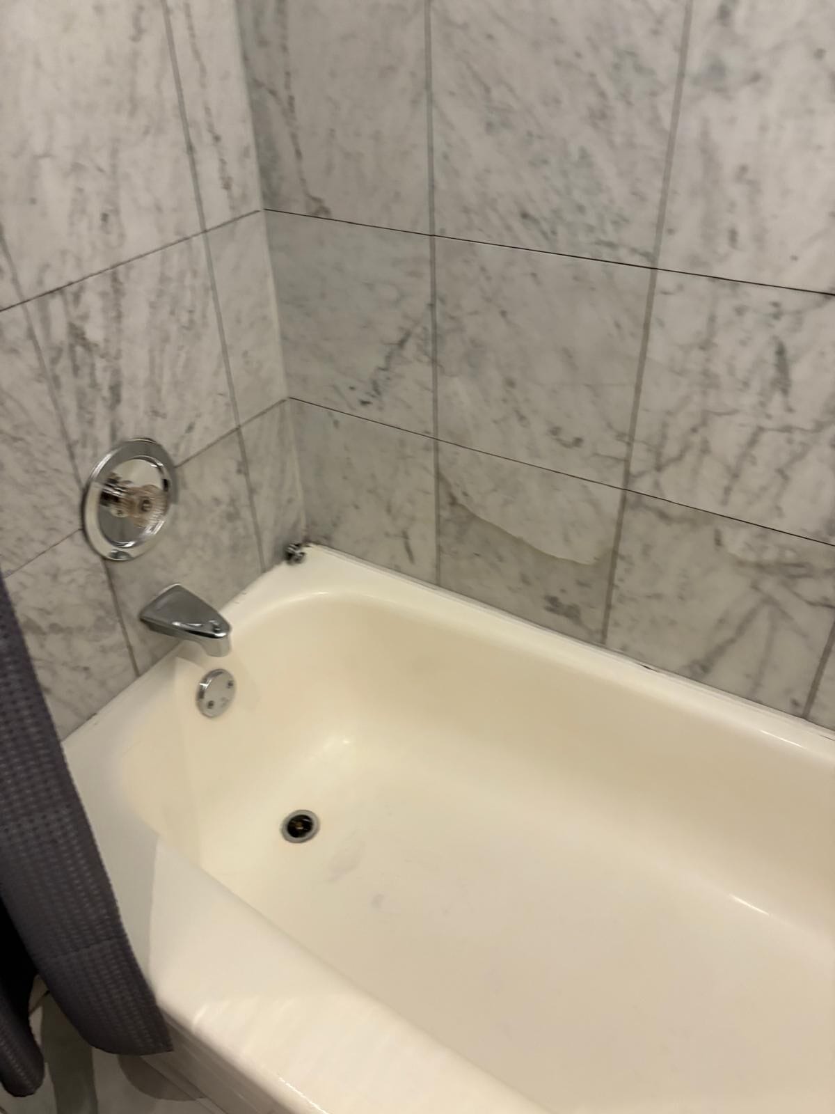 A bathroom with a white bathtub, a chrome faucet, and a marble tiled wall.