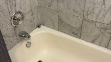 A bathroom with a white bathtub, a chrome faucet, and a marble tiled wall.
