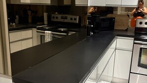 Una cocina moderna con armarios blancos, encimera negra y electrodomésticos de acero inoxidable.