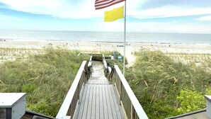 Een houten looppad dat naar een strand leidt, met een Amerikaanse vlag en een gele vlag op een paal.