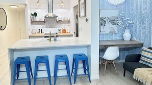 Een moderne keuken met witte kasten, een centraal eiland met blauwe barkrukken, en een eetgedeelte met een patroonmuur en een wereldbol.