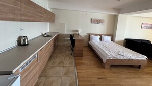 Ett kompakt hotellrum med ett litet kök, en säng och ett skrivbord.
