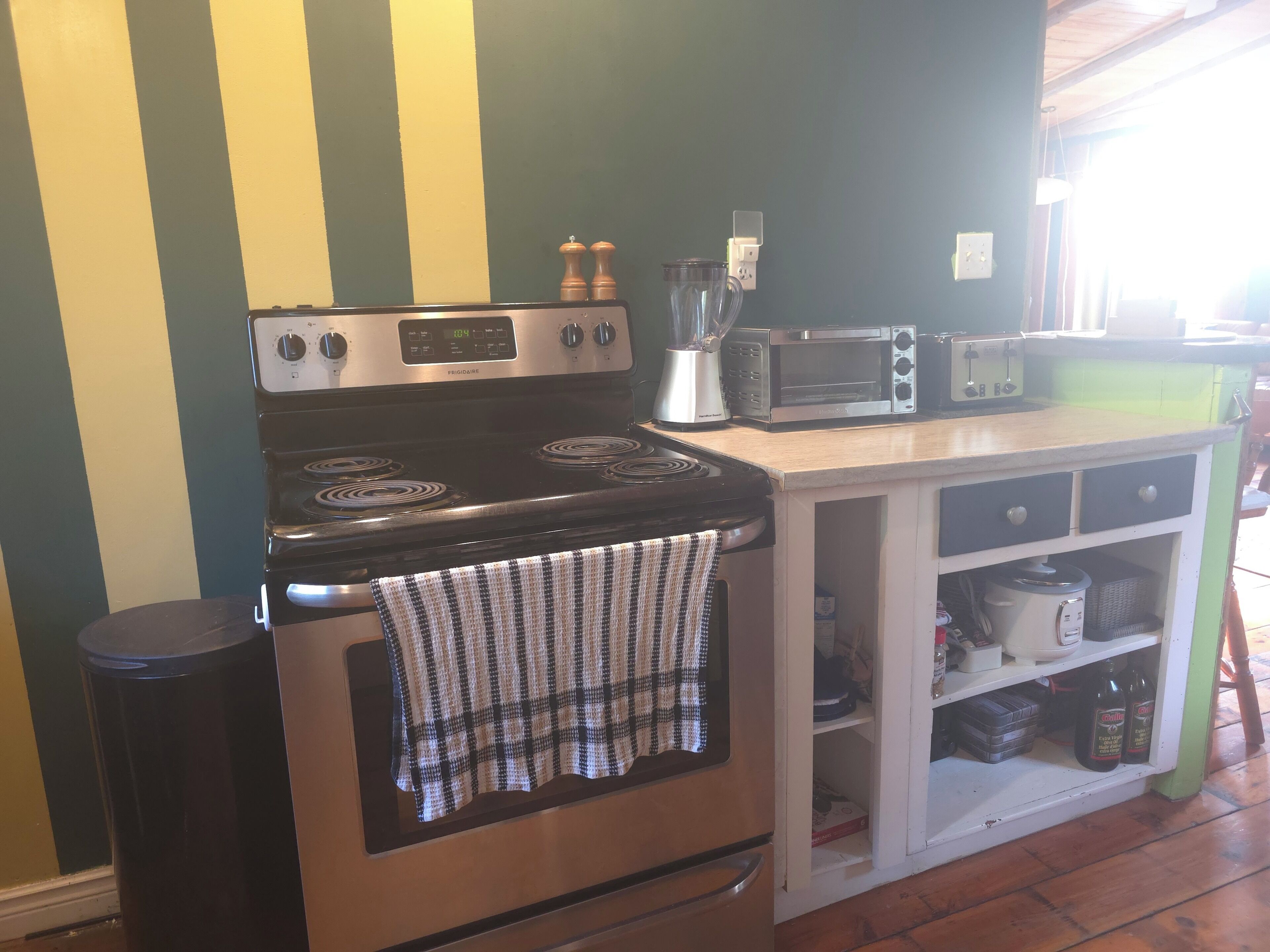 Una cocina con estufa, tostadora y licuadora sobre la encimera.
