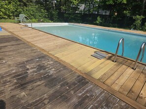 A wooden deck with a swimming pool, metal handrails, and a green chair. - Cozy cottage w/fire pit &waterview, close to parlee beach and amenities. (Shédiac)