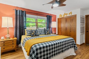 A bedroom with a bed, curtains, a nightstand, a lamp, a wardrobe, and a wall sign.