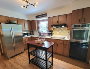 A modern kitchen with stainless steel appliances, wooden cabinets, and a central island with a basket. - Tranquil - North Porch Cottage - New AC - KING & QUEEN beds (Ellison Bay)