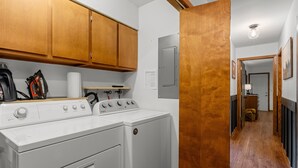 A laundry area with two white front-loading washing machines, wooden cabinets, and a visible door leading to another room. - Tranquil - North Porch Cottage - New AC - KING & QUEEN beds (Ellison Bay)