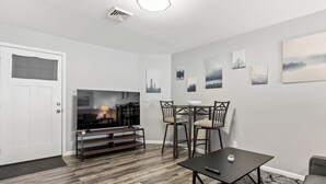 A modern living room with a flat-screen TV, a dining table with chairs, and artwork on the walls. - Central Festus Studio Apartment. Private Parking-Gigabit Wifi-Full Size Kitchen. (Festus)