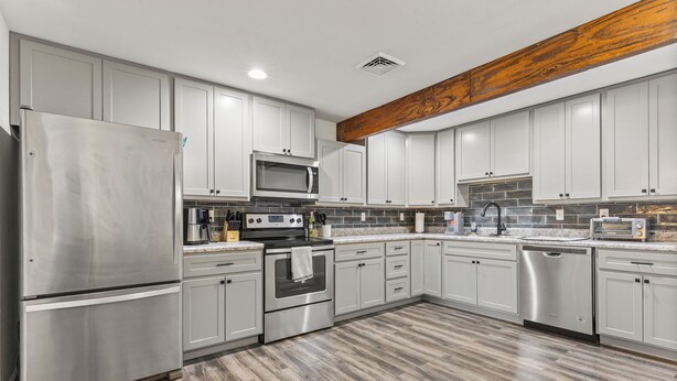 A modern kitchen with stainless steel appliances, white cabinets, and a wooden beam ceiling. - Central Festus Studio Apartment. Private Parking-Gigabit Wifi-Full Size Kitchen. (Festus)
